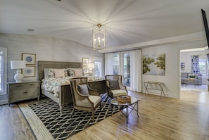 Une chambre à coucher moderne avec un grand lit, deux fauteuils, une petite table et des œuvres d’art accrochées aux murs.