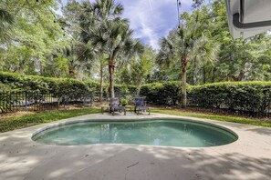 A swimming pool surrounded by lush greenery and a black metal fence.