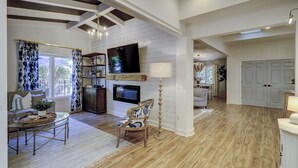 Uma sala de estar espaçosa com lareira, televisão e área de jantar com mesa de vidro.