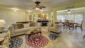 A spacious living room with a sofa, armchairs, a coffee table, and a dining area with a table and chairs. There is a kitchen in the background with wooden cabinets and a microwave. - Sunset Rentals | Bradley Circle 9 | Dog Friendly (Hilton Head Island)