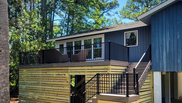 A two-story wooden deck with a black railing, a staircase, and a window overlooking a wooded area. - Sunset Rentals | Bradley Circle 9 | Dog Friendly (Hilton Head Island)