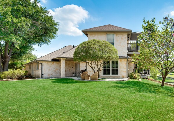 A two-story house with a well-maintained lawn, a large tree in front, and a small porch with outdoor furniture. - Sprawling Resort Oasis with Heated Pool Set up for Groups (Plano)