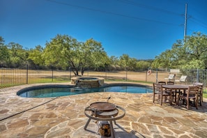 A stone pool with a hot tub, surrounded by a fence and trees.