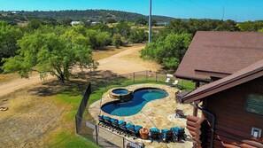 Una piscina con cubierta de piedra, rodeada por una cerca, y una cabaña de madera con tejado de ladrillo.