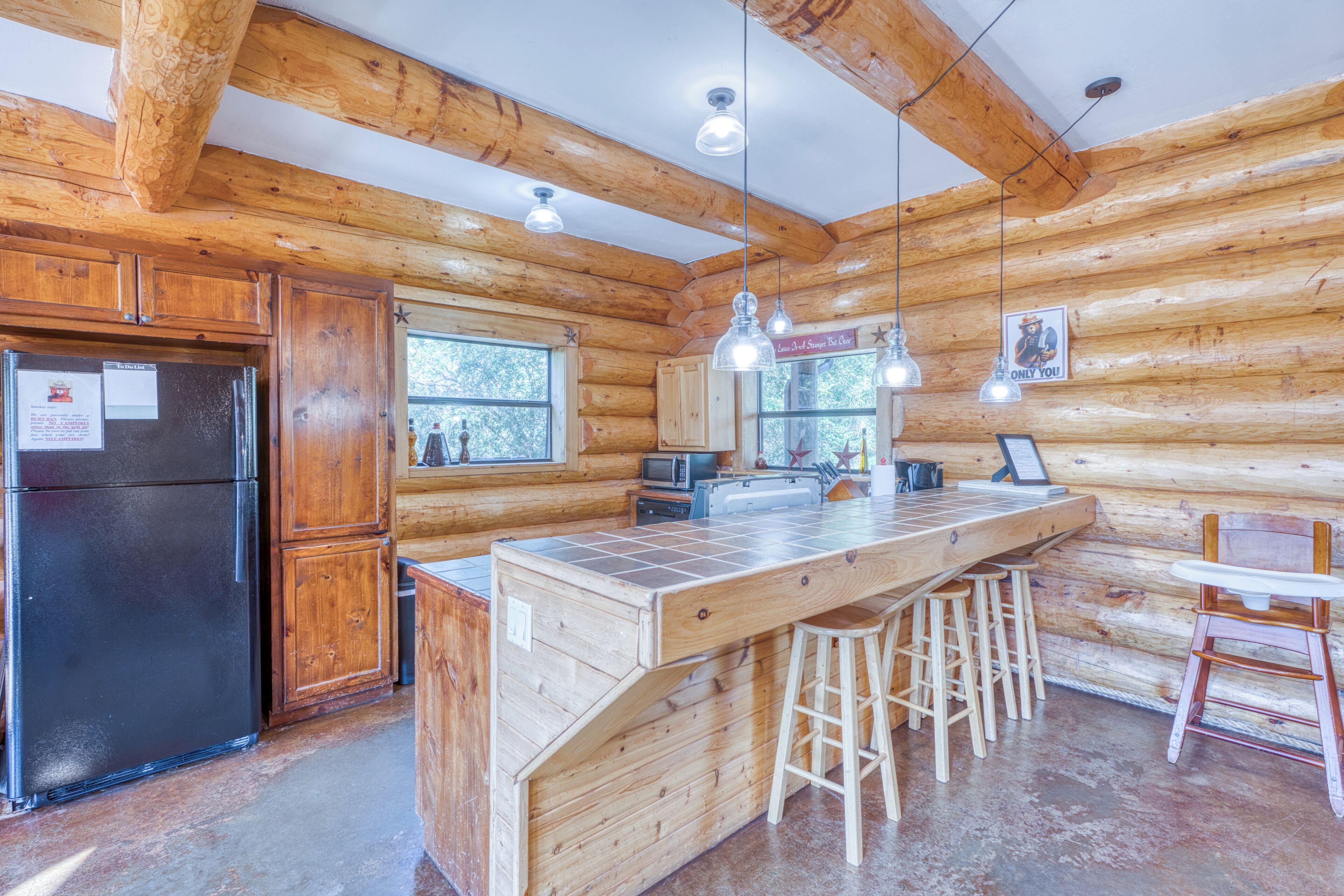 A wooden cabin interior with a kitchen area featuring a refrigerator, a sink, and bar stools.