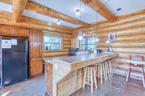 A wooden cabin interior with a kitchen area featuring a refrigerator, a sink, and bar stools.