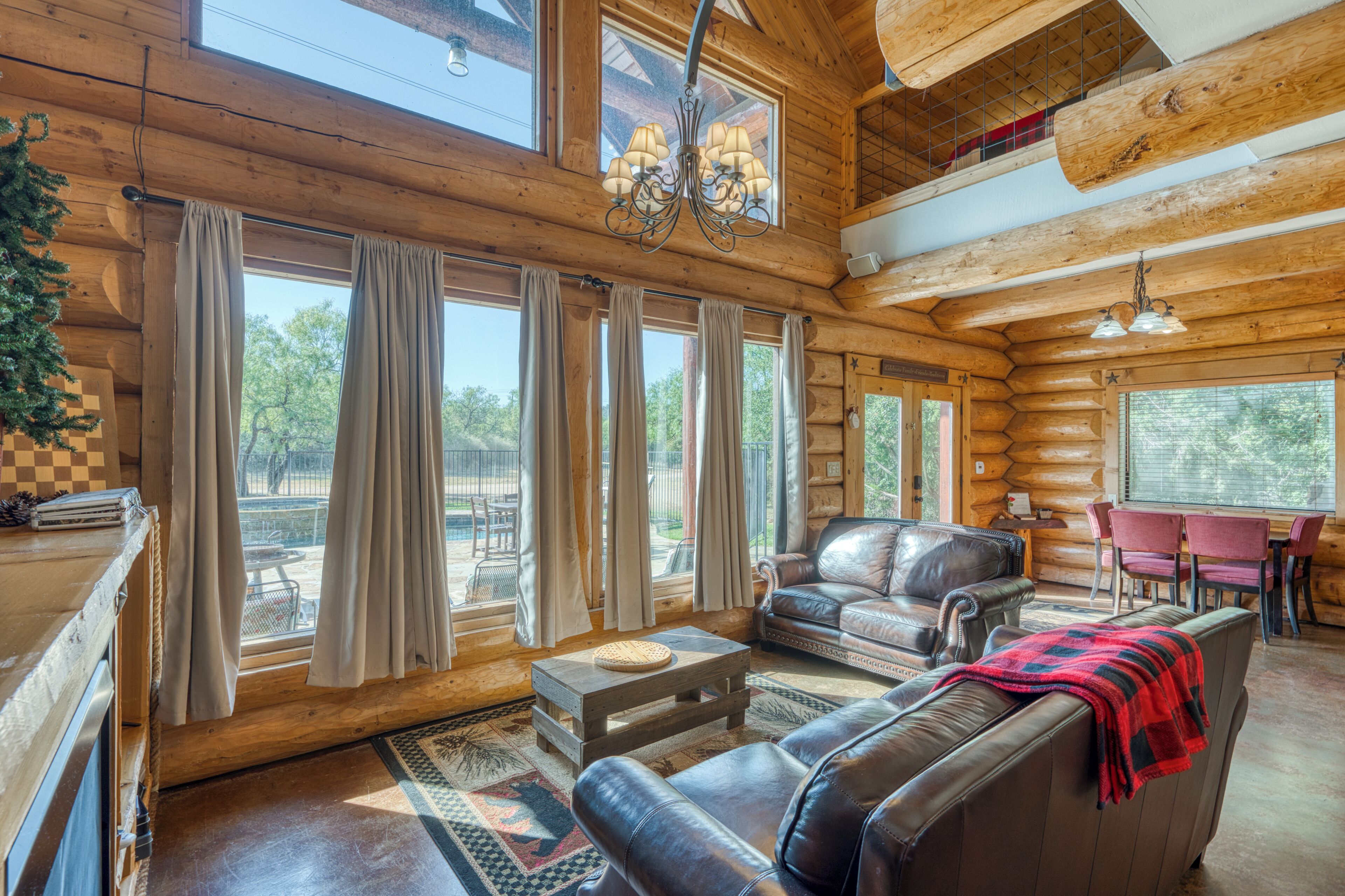 A log cabin interior with a dining area, leather sofas, and a chandelier.