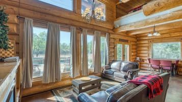 A log cabin interior with a dining area, leather sofas, and a chandelier.