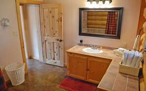 A bathroom with a wooden door, a sink, a mirror, and a red rug.