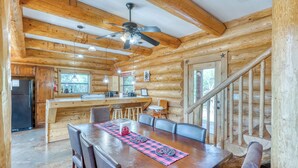 Interior de una cabaña de madera con comedor, cocina y una escalera.