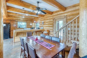 A wooden cabin interior with a dining area, kitchen, and a staircase.