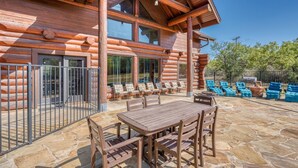 A log cabin with a patio area featuring a stone floor, wooden table and chairs, and a seating area with blue cushioned chairs.