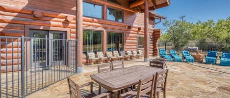 A log cabin with a patio area featuring a stone floor, wooden table and chairs, and a seating area with blue cushioned chairs.