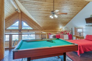 A cozy room with a pool table, a bed with red bedding, and a ceiling fan. - Private Pool, Hot Tub & Games Near Lake LBJ | Pet Friendly, Sleeps 14 (Burnet)
