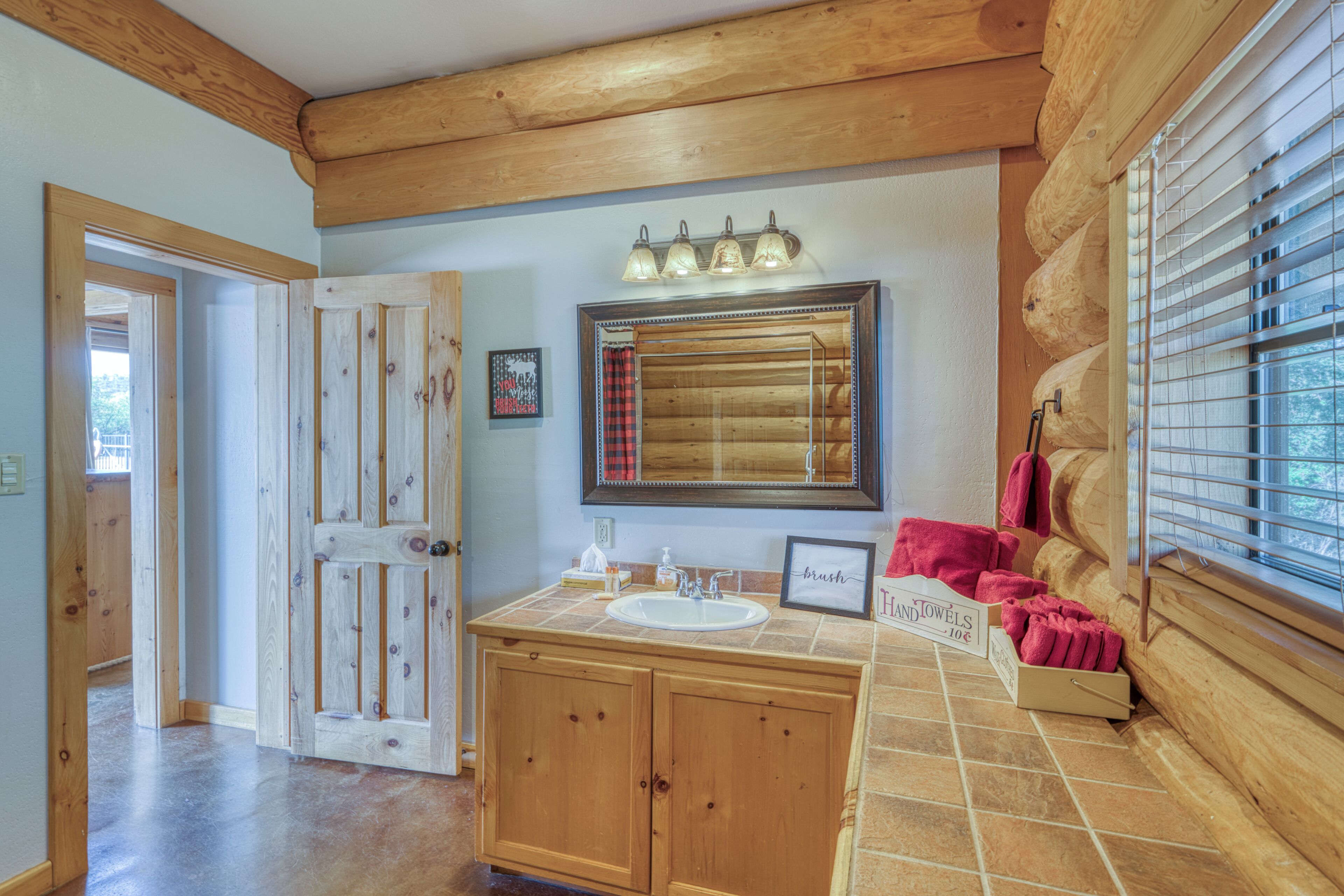 Une salle de bain avec des meubles en bois, un lavabo, un miroir et une fenêtre avec des stores.