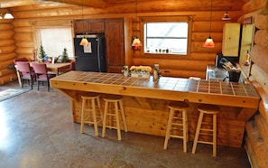 Interior de una cabaña de madera con cocina que incluye una isla grande con taburetes, un refrigerador y una ventana con vistas.
