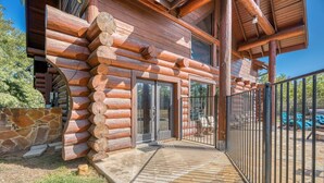 A log cabin with a stone foundation, a wooden deck, and a metal fence.