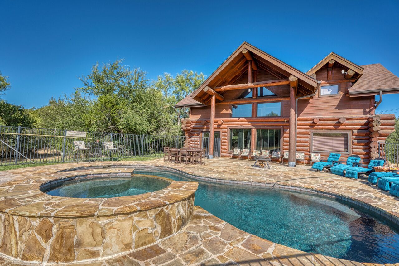 A log cabin with a hot tub and stone patio.