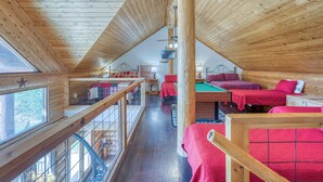 A wooden cabin with a loft bedroom, a pool table, and a balcony with a railing.