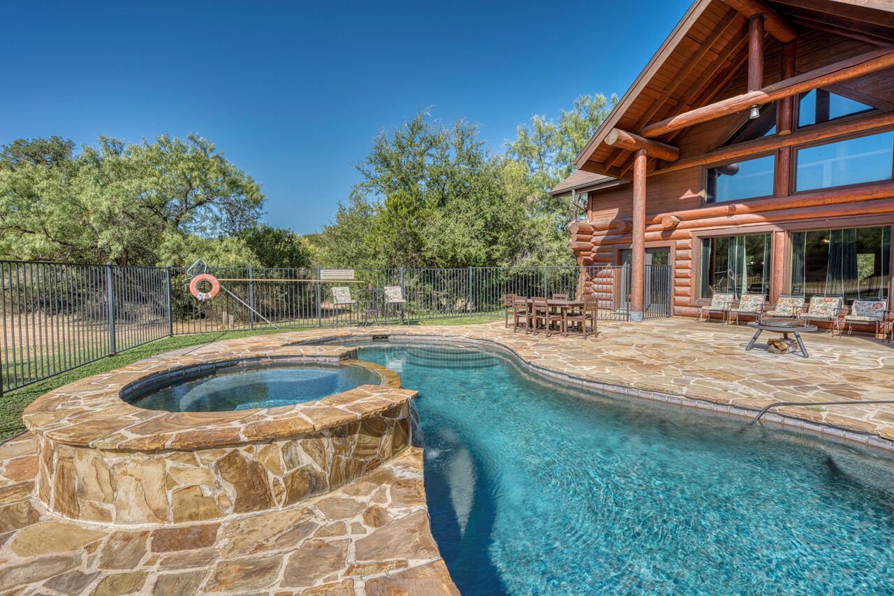 Una piscina con hidromasaje, rodeada por una terraza de piedra, y una cabaña de madera con ventanas amplias.