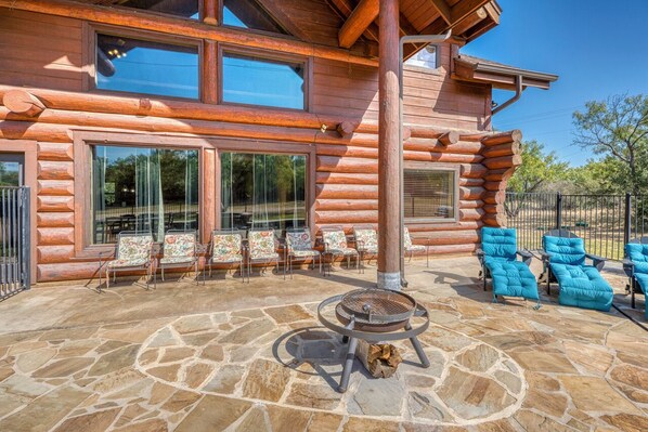 Una cabaña de troncos con un patio de piedra, mobiliario exterior y una parrilla.