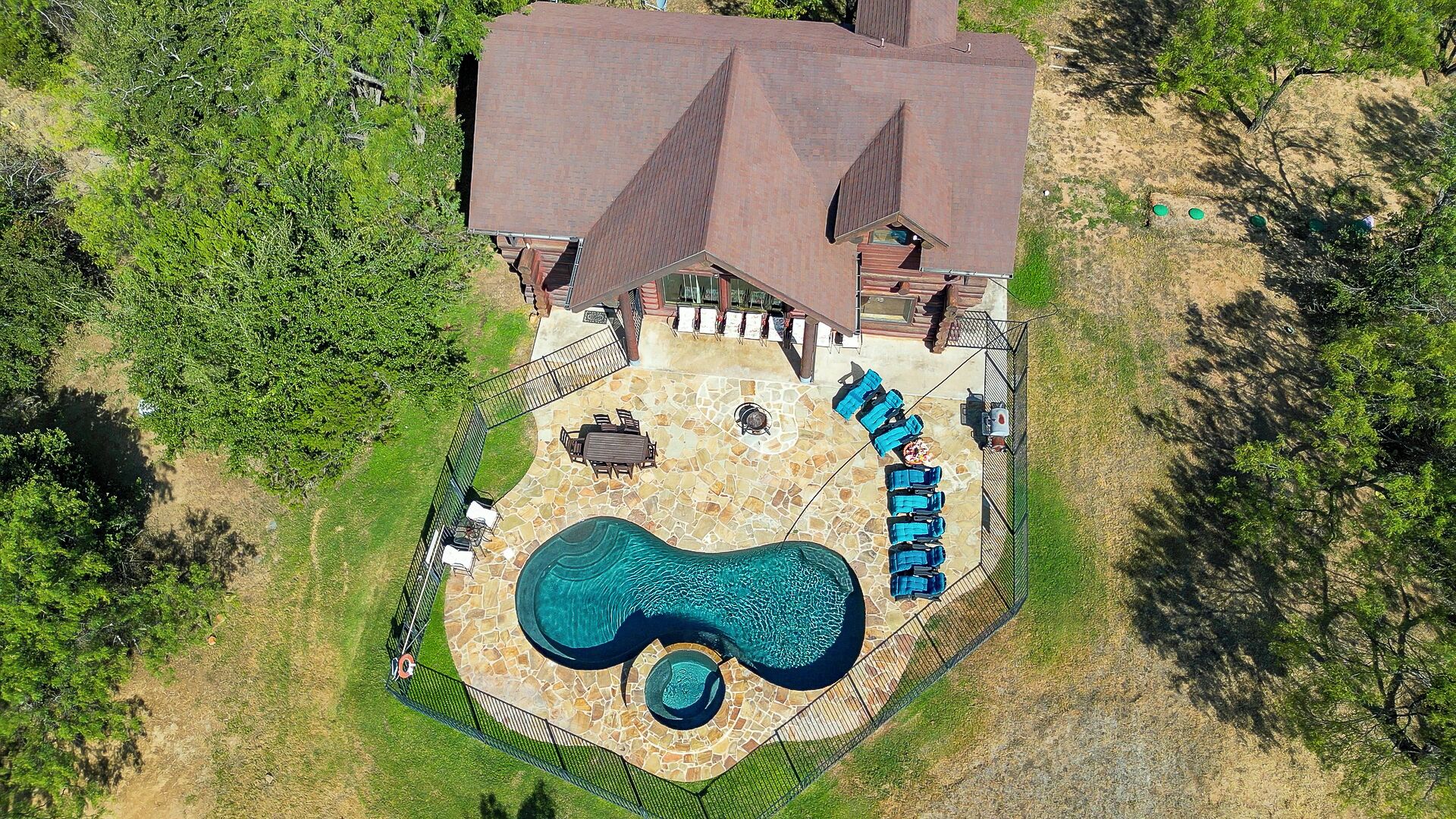 An aerial view of a house with a swimming pool, patio furniture, and a fenced yard.