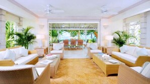 A spacious room with wicker furniture, a central coffee table, and a view of a tropical outdoor area. - Secret Cove 4 (Derricks)
