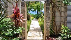 A stone pathway flanked by lush greenery and a wooden pergola. - Secret Cove 4 (Derricks)