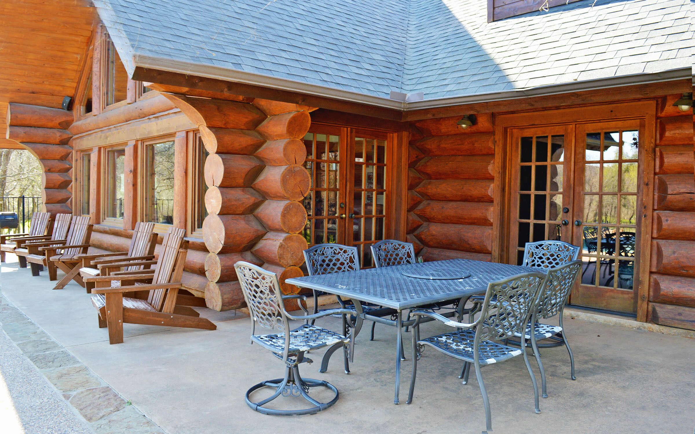 A log cabin with a patio featuring a table and chairs, a fire pit, and a view of the surrounding forest.