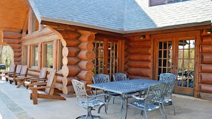 Eine Blockhütte mit einer Terrasse, die einen Tisch, Stühle, eine Feuerstelle und einen Blick auf den umliegenden Wald bietet.