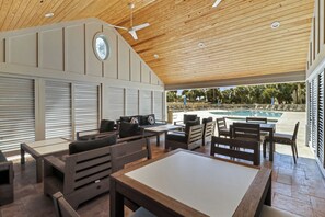 An outdoor patio with wooden furniture, a ceiling fan, and a view of a swimming pool.