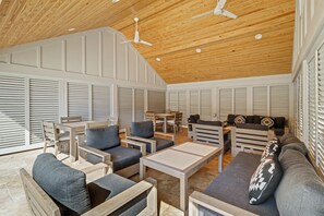 A spacious room with a high wooden ceiling, built-in ceiling fans, and a large window with blinds. There are multiple seating areas with sofas and chairs. - Sunset Rentals | Captains Walk 458 (Hilton Head Island)