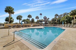 A rectangular swimming pool with a tiled deck, surrounded by lounge chairs and palm trees.