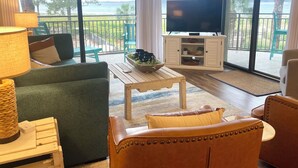 A living room with a sofa, a coffee table, a TV on a cabinet, and a view of the outdoors. - Sunset Rentals | Beachside Tns 1870 (Hilton Head Island)
