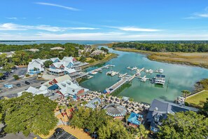 An aerial view of a marina with boats docked, a parking lot, and buildings with blue roofs. - Sunset Rentals | Beachside Tns 1870 (Hilton Head Island)