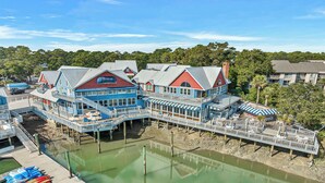 A waterfront property with multiple buildings, a dock, and a greenish water body. - Sunset Rentals | Beachside Tns 1870 (Hilton Head Island)