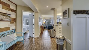 A hallway with a wooden bench, a trash bin, and a door leading to a bedroom with a bed and a window. - Sunset Rentals | Beachside Tns 1870 (Hilton Head Island)