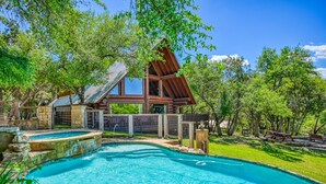 A wooden cabin with a swimming pool, surrounded by trees and a fenced yard.