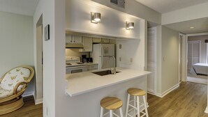 Une cuisine moderne avec des armoires blanches, un évier en acier inoxydable et deux tabourets de bar.