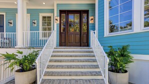 A two-story house with a front porch, a wooden front door, and a staircase leading to the entrance. - Sunset Rentals | Egret 5 (Hilton Head Island)