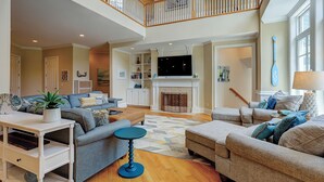 A spacious living area with a high ceiling, a fireplace, and a television. - Sunset Rentals | Egret 5 (Hilton Head Island)