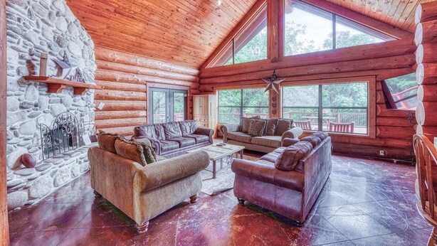 Un intérieur spacieux de chalet en bois, avec plusieurs coins salon, de grandes fenêtres et un mur en pierre.