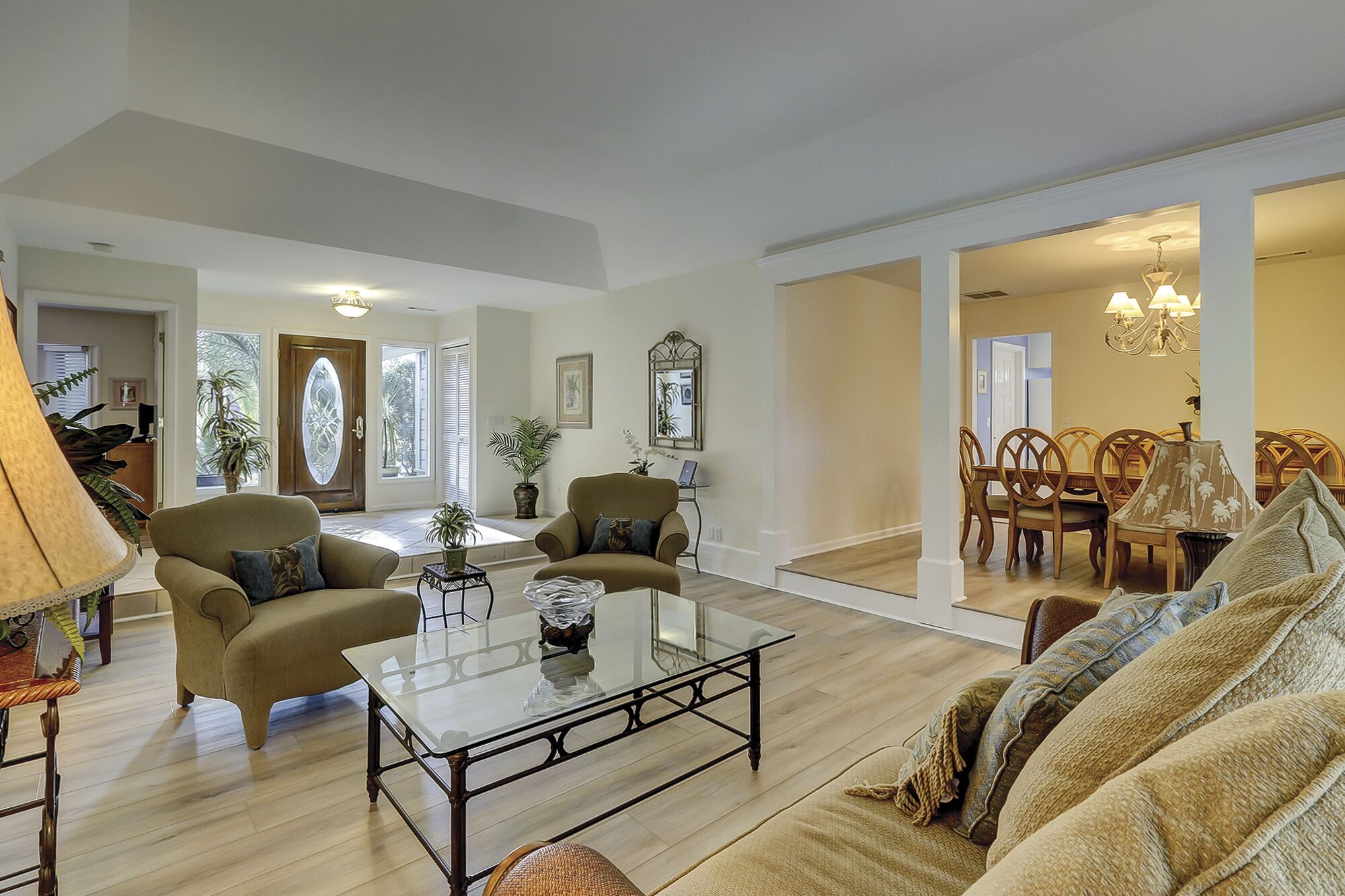 A spacious living room with a glass coffee table, comfortable seating, and a dining area with wooden chairs.