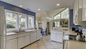 A modern kitchen with white cabinetry, a large island, and a dining area with chairs. - Sunset Rentals | Baynard Park 6 | Dog Friendly (Hilton Head Island)