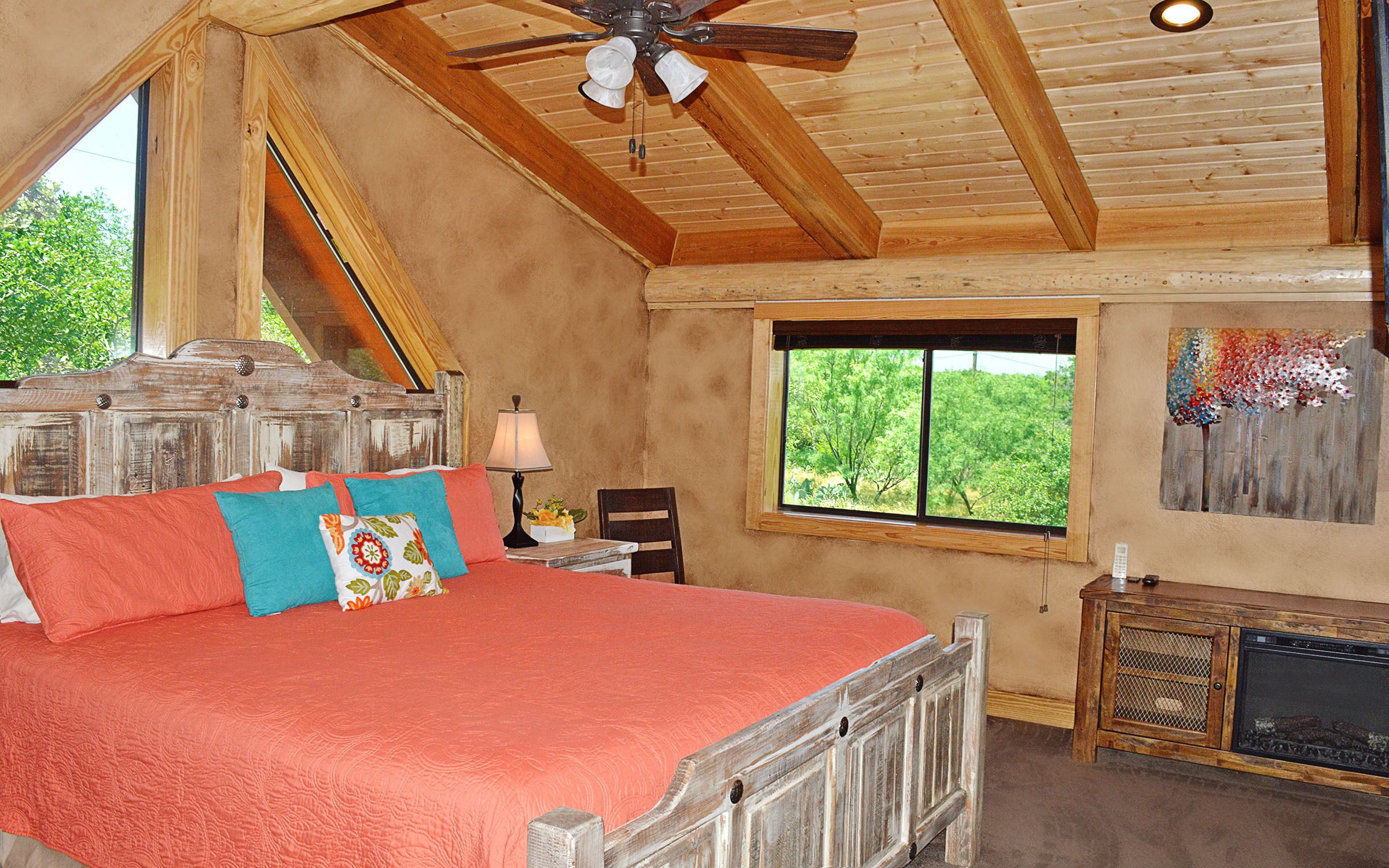 A bedroom with a large bed, wooden ceiling beams, a window with a view, and a fireplace.