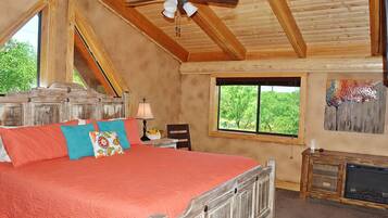 A bedroom with a large bed, wooden ceiling beams, a window with a view, and a fireplace.