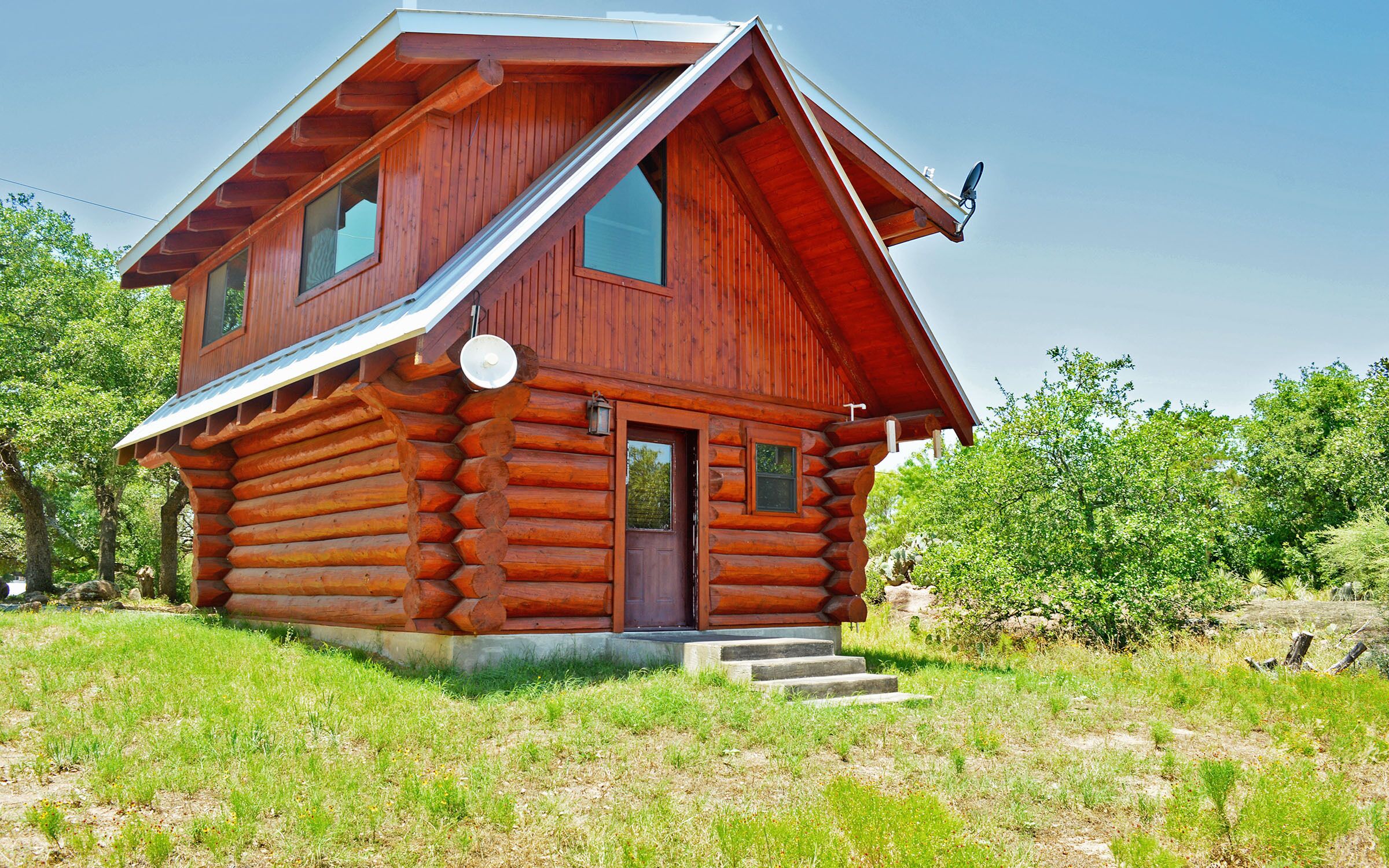 A log cabin with a steeply pitched roof, a front porch, and a satellite dish.