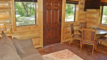 A log cabin interior with a wooden door, a dining table with chairs, a sofa, and a rug.