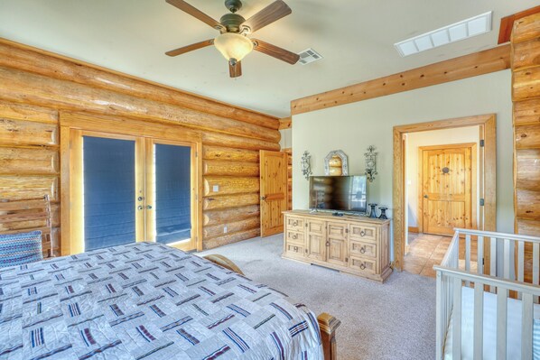 A log cabin bedroom with a bed, dresser, and a ceiling fan.