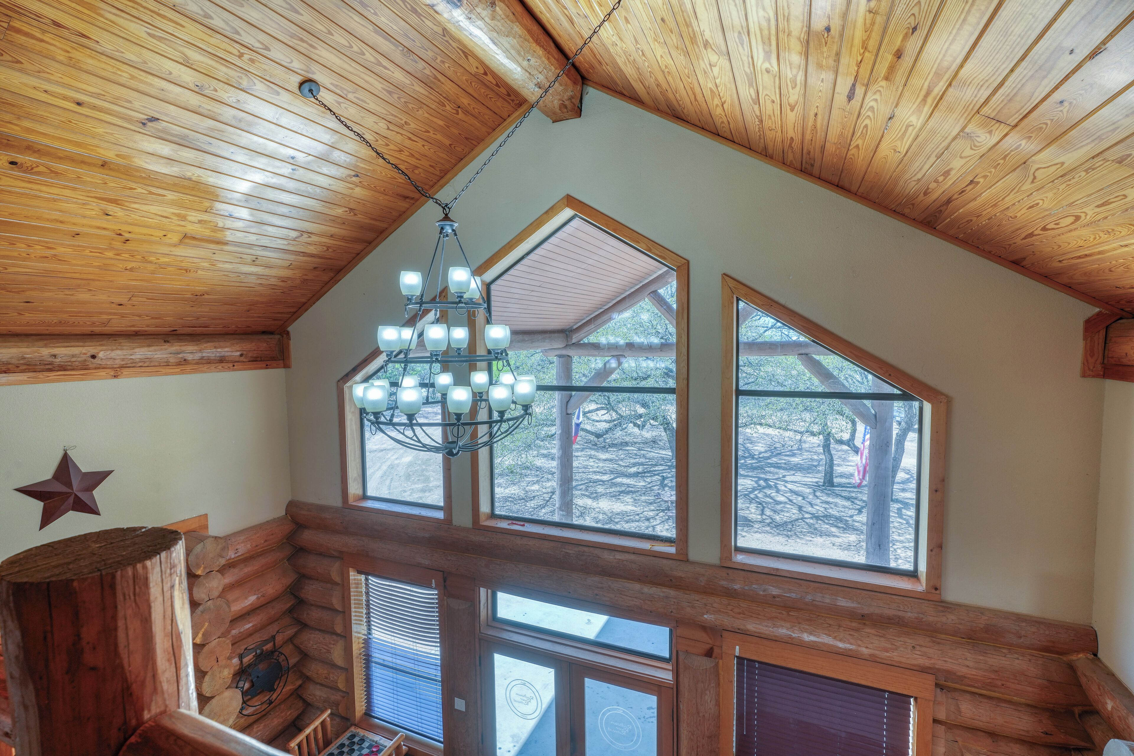 A log cabin interior with a sloped ceiling, large windows, and a chandelier.